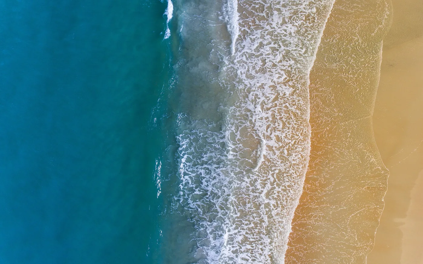 Aerial view of clear turquoise water meeting open sand